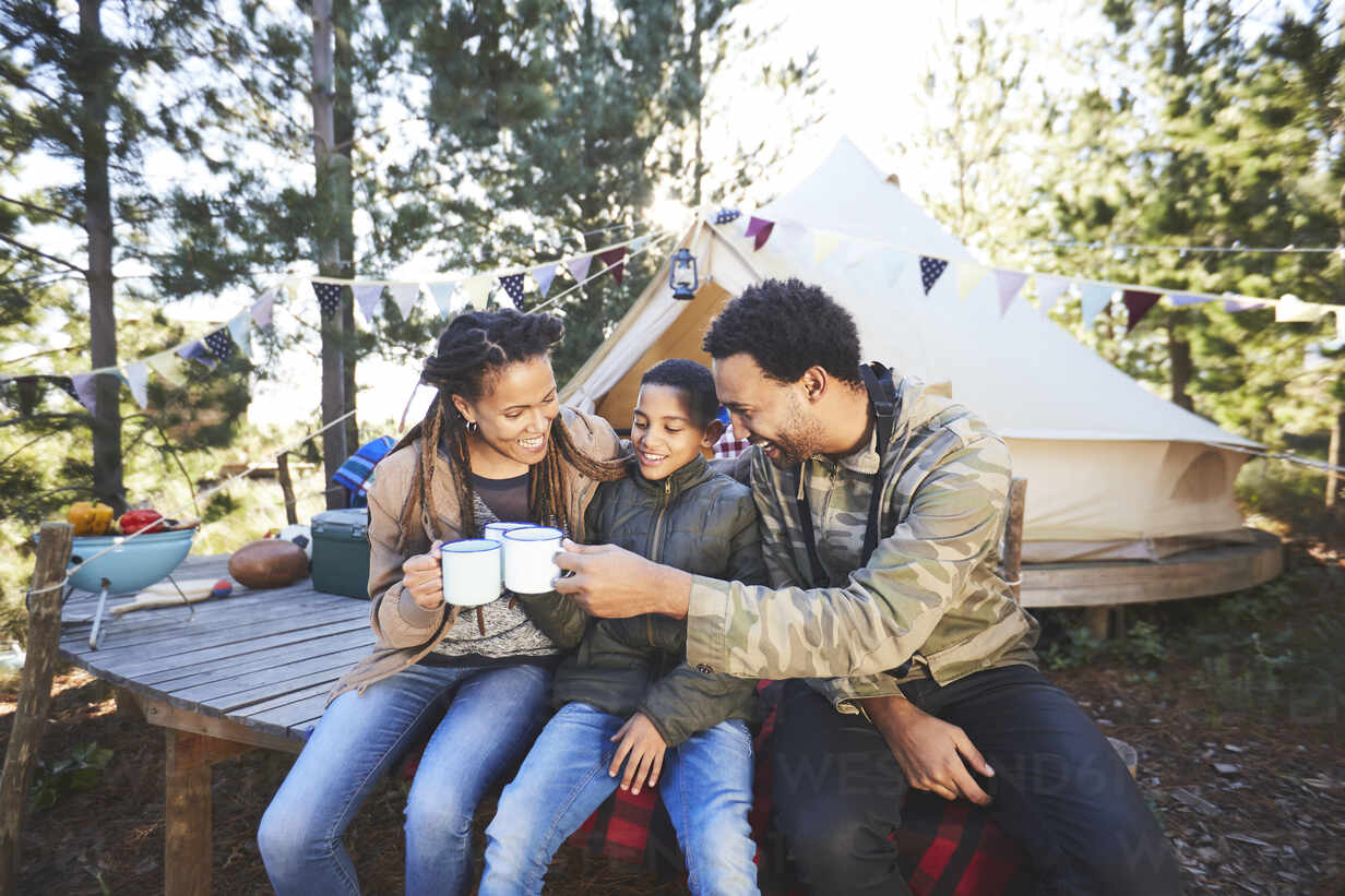 Happy family drinking coffee and hot chocolate at campsite in woods