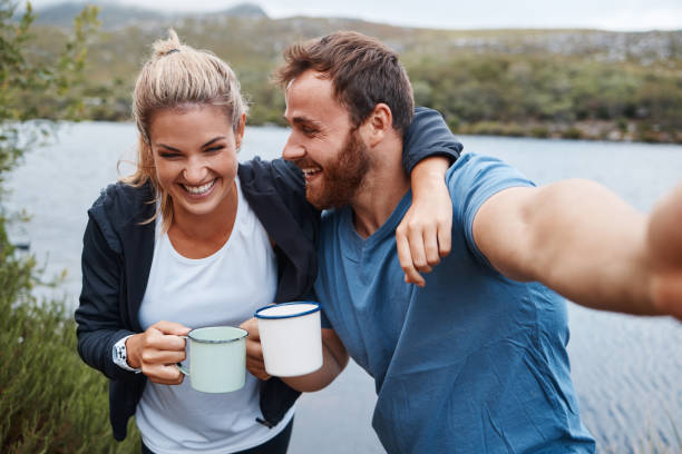 Nature, camping and selfie couple with coffee drink happy with adventure vacation at Mexico lake. Holiday, relax and happiness of people enjoying warm beverage in camper mug photograph.